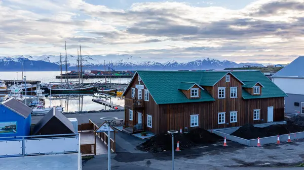 Husavik, İzlanda, 21.05.22. Liman manzaralı Husavik manzarası, geleneksel İzlanda mimarisi ve kar kaplı Viknafjoll ve Kinnarfjoll dağ sıraları arka planda, kutup gecesi.