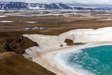 Krafla Kalderası 'ndaki Viti patlaması krateri turkuaz su, kar ve buz dolu, arka planda otopark ve dağ manzaralı, Myvatn Jeotermal Alanı, İzlanda.