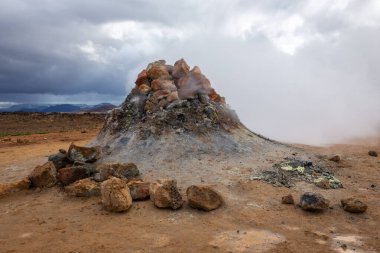 Fuming borehole, simmering and steaming volcanic vent in Hverir, Myvatn Geothermal Area in Iceland, with volcanic landscape in the background. clipart