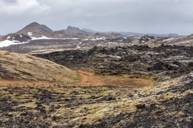 İzlanda, Myvatn Jeotermal Bölgesi 'ndeki Leirhnjukur volkanı kara lav tarlaları, arka planda yosun ve dağlarla kaplanmış donmuş magma..