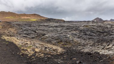 İzlanda, Myvatn Jeotermal Bölgesi 'ndeki Leirhnjukur volkanı kara lav tarlaları, arka planda yosun ve dağlarla kaplanmış donmuş magma..