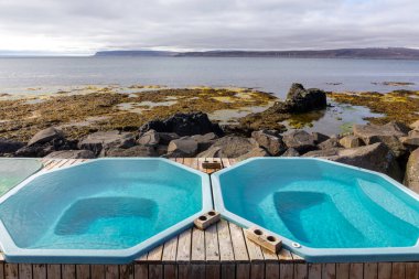 Drangsnes jakuzileri, deniz kenarındaki jeotermal havuzlar Westfjords, İzlanda 'daki Drangsnes köyü, arka plandaki kayalık kıyı ve dağlar..