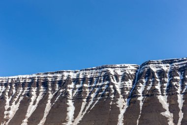 Isafjordur, Westfijords, İzlanda 'da couloir' larla kaplı karla kaplı lav dağı tepesi. Arka planda mavi gökyüzü, kopyalama alanı..