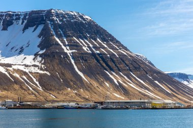 Isafjordur, İzlanda, 23.05.22. Karla kaplı volkanik dağ sırasının eteklerindeki yat, gemi, nakliye ve lojistik tesisleri ve hangarlarla dolu güvenli Ürdün limanı..