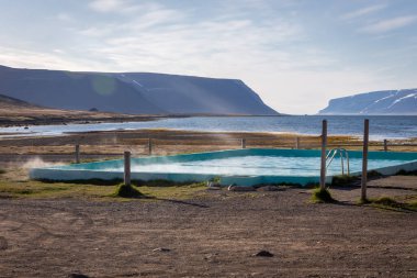 Reykjafjardarlaug Sıcak Jeotermal Havuzu buharlı turkuaz su ve Westfijords manzaralı karlı dağlar ve İzlanda körfezi, insan yok..