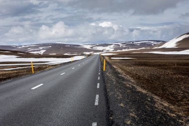 Çevre yolu (1. Yol) Doğu İzlanda 'da düz asfalt yol, karla kaplı volkanik dağlar, kenarlarında sarı yol işaretleri var..