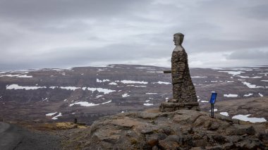 Westfjords, Iceland, 24.05.2022. Kleifabui man statue at Kleifaheidi pass, cairn erected by road workers in 1947 with Westfjords mountain landscape in the background. clipart