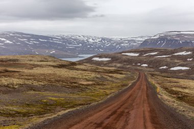 Patreksfjordur, Westfjords, İzlanda 'da karla kaplı engebeli dağlardan geçen toprak yol..