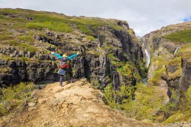 Hvalfjordur, Vesturland, İzlanda 'daki Glymur şelalesi kadın yürüyüşçü turistin uçurumun kenarında durduğu manzara.