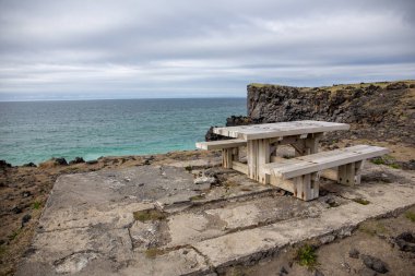 Picnic area with wooden table and bench by the Skardsvik Beach on Snaefellsnes peninsula in Iceland with sea view and volcanic cliffs. clipart