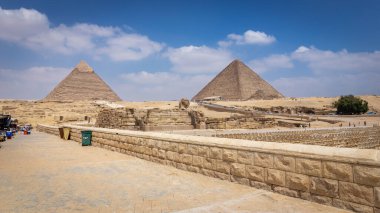 Piramit Kompleksi, Sfenks ve kazıları olan Giza Platosu manzarası, sandalyeli açık hava tiyatrosu, hediyelik eşya pazarı tezgahları olan turistler için yürüme yolu, Mısır.