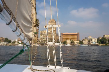 Giza, Mısır, 25.07.21. Nil Nehri 'ndeki geleneksel ahşap yelkenli. Doğal pamuklu yelkenli, halat ve teçhizatlı. Nasser' ın konut binasıyla Giza manzaralı..