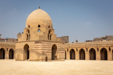 Mısır 'ın Kahire kentindeki İbn Tulun Camii, avlu manzarası ortasında kubbeli büfe çeşmesi ve etrafındaki sütunlar ve kemerler oyulmuş sıva ile süslenmiş..