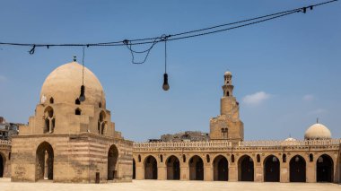 Kahire, Mısır 'daki İbn-i Tulun camii, kubbeli kiosk çeşmesi, spiral minare ve etrafındaki sütunlar ve kemerler oyulmuş sıva, asılmış ampullerle süslenmiş avlu manzarası..