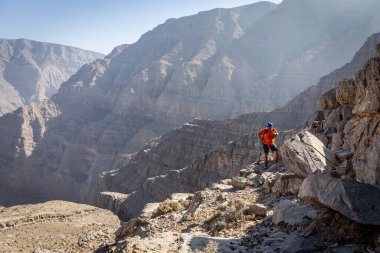 Yürüyüş direkleri ve sırt çantasıyla erkek yürüyüşçü Wadi Ghalilah 'tan Hajar dağlarındaki Jebel Jais tepesine kadar Cennete giden merdivenlerde tırmanıyor..