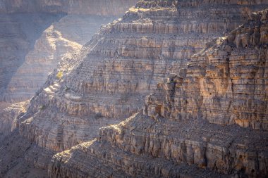 Güneş tarafından aydınlatılan kaya oluşumları ve katmanlar, Hajar Dağları 'ndaki çatlak, kuru ve kayalık çöl yamacının yakın görüntüsü, Ras al Khaimah, BAE.