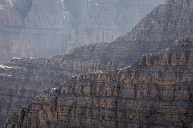 Güneş tarafından aydınlatılan kaya oluşumları ve katmanlar, Hajar Dağları 'ndaki çatlak, kuru ve kayalık çöl yamacının yakın görüntüsü, Ras al Khaimah, BAE.