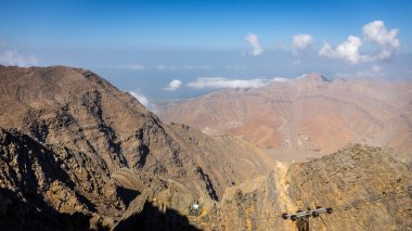 Hajar Dağları kayalık tepeleri, Wadi Ghalilah çiftlik köyü, yamaçtaki elektrik direkleri, Basra Körfezi manzarası, Ras al Khaimah Emirliği, BAE.
