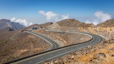 Jebel Jais Zirvesi 'ndeki sarmal asfalt yolda Ras al Khaimah, Birleşik Arap Emirlikleri otoparkı ve binaları ile kayalık Hajar sıradağları.