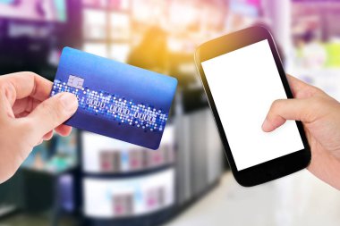 Woman with hand holding smart phone with Credit Card over blurred of cosmetic shop.