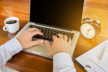 Young businessman using his laptop with black coffee, clock,analyze graph plans.
