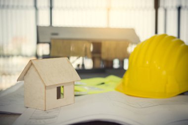 Selective focus of Ardboard house with helmet Construction plans ,pem and blueprints on wooden table with sunshine background.