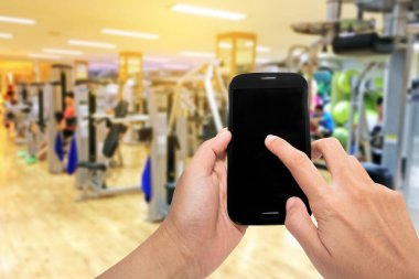 Hand holding smartphone device with sunshine at motion  blur gym background