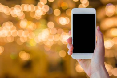 Woman hand holding empty screen of smart phone with blur festive gold bokeh background.