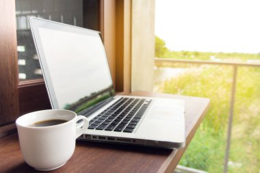 Kahve fincanının seçici odak noktası ve yeşil doğal arka planı olan koyu ahşap bir laptop..