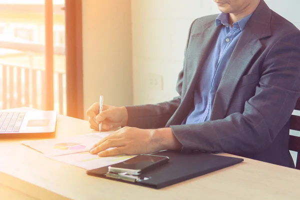 Business man working at office with laptop and documents near the window and sunshine background.