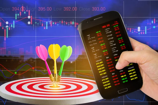 Hand holdind smartphone and stock charts screen with target center of dartboard with sunshine background,competitive business concept,organization that has potential to be lead the business