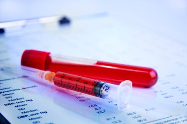 Hematology blood analysis report with blood sample collection tubes and syringe. (blue tone)