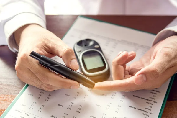 close up of men hands using lancet on finger to check blood sugar level by Glucose meter on chart background.(vintage tone