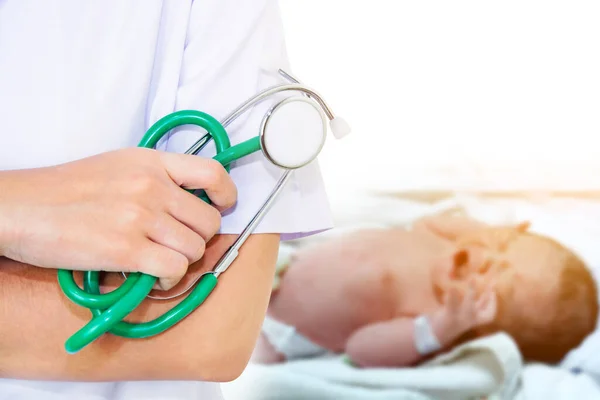 Doctor with green stethoscope with motion blur of newborn baby crying on the bed with sunshine background.