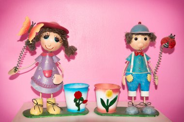 Girl and boy dolls clay with flower pot on pink wall background.