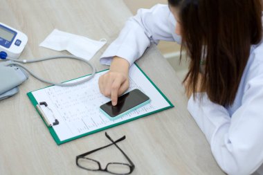 Doctor reading smartphone on a chart at office in the hospital. Medical and healthcare concept.