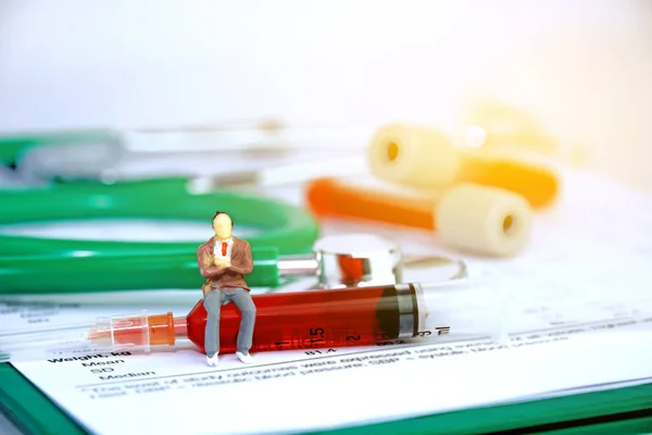 Küçük oyuncak doktor, yeşil steteskop, test tüpü, kan plazması ve beyaz arka planda şırınga olan tıbbi belgeler..