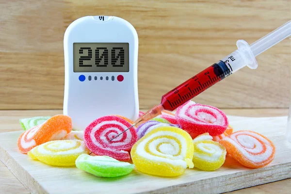 Glucose meter with word diabetes candy dessert  too many sweets, unhealthy food, concept of diabetes and reduction of eating sweets with syringe.