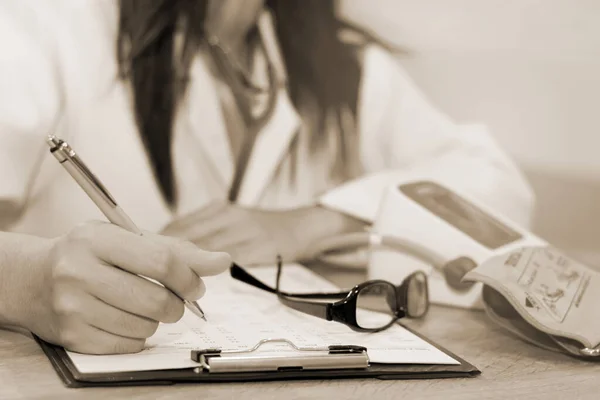 Close-up of a female doctor in office filling out application form with smartphone , sitting at the table in the hospital.(grayscale tone)