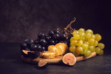 Tahtadaki siyah ve beyaz üzüm kümeleri koyu bir arka planda.