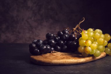 Tahtadaki siyah ve beyaz üzüm kümeleri koyu bir arka planda.