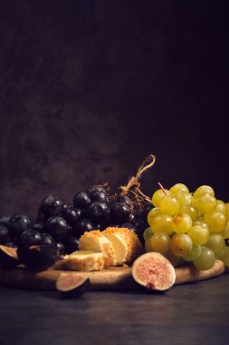 Tahtadaki siyah ve beyaz üzüm kümeleri koyu bir arka planda.