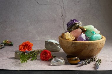 Gri arka planda ahşap bir kasede çeşitli değerli taşlar var.