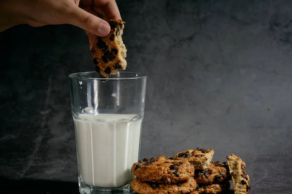 hand soaks chocolate biscuits in a glass of milk