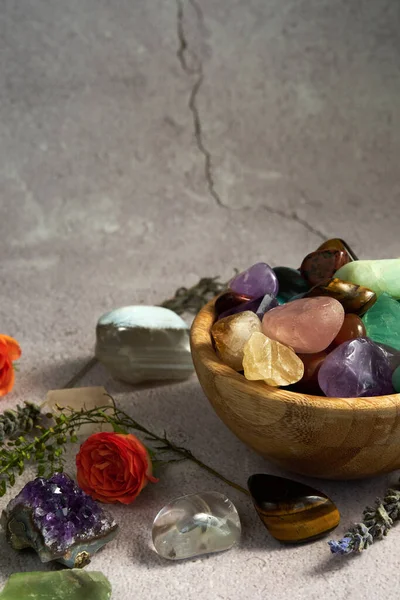 various gem stones in a wooden bowl on a gray background
