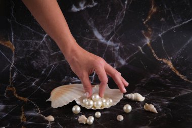 İnciler bir kabukta koyu bir arka planda ve masanın üzerine saçılmıştır.