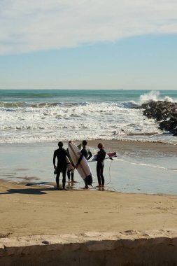 Sahilde sörf tahtası olan bir grup sörfçü dalgaların arka planında