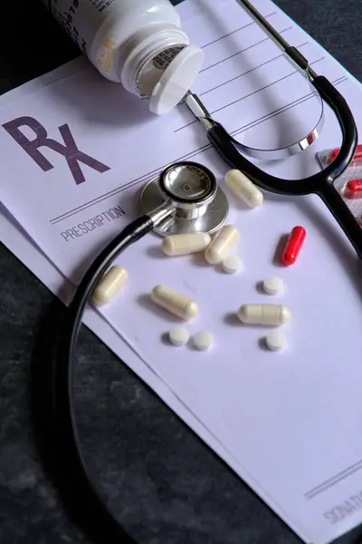 medical stethoscope blank prescription sheet and scattered pills on dark background