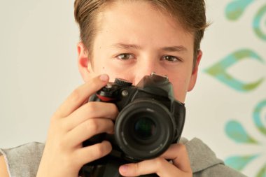 Beyaz arka planda elinde kamera olan bir çocuğun portresi.