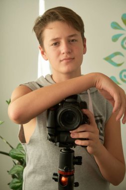 Beyaz arka planda elinde kamera olan bir çocuğun portresi.